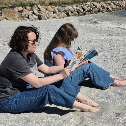To bibliotekarer sidder på en strand og læser i hver sin bog